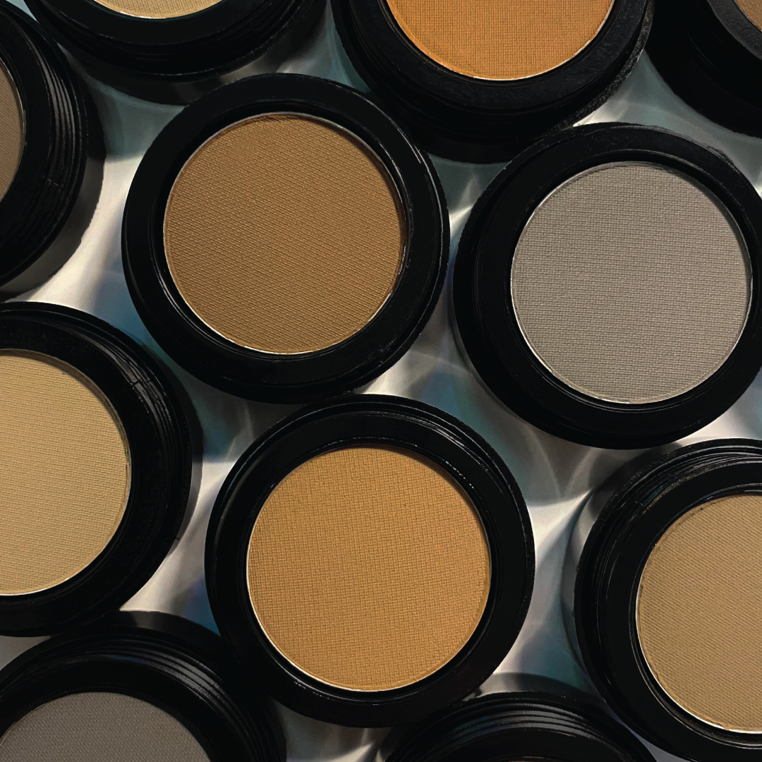 Six unbranded brow powder pots in assorted shades on a pale blue surface